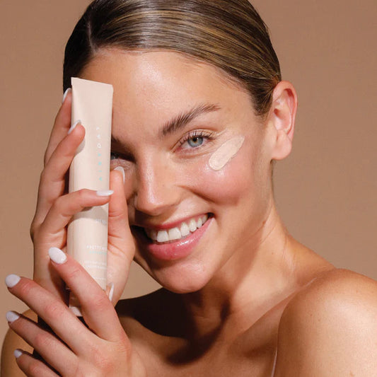 Woman applying spf50+ to her face with a beige background