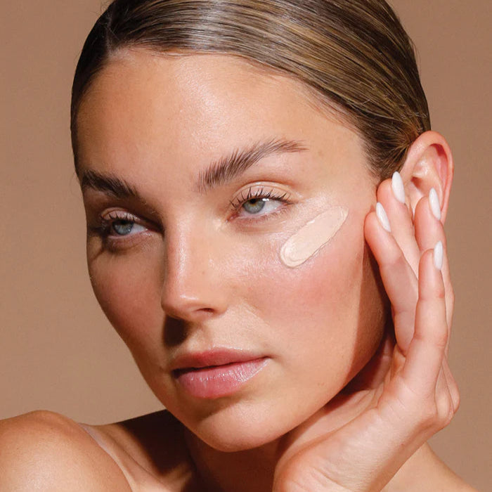 Woman applying cream to her face with a neutral background